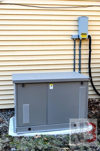 Standby generator installed on a concrete pad beside a home with an exterior transfer switch and conduit
